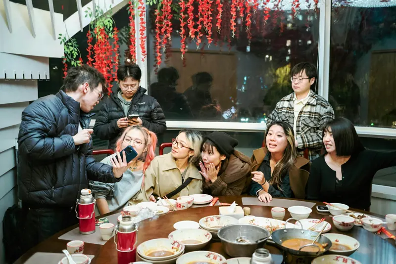 一班朋友圍住圓枱食飯，有人拎起手機影相，窗邊掛住紅燈籠